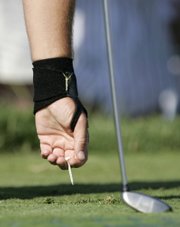 PHIL MICKELSON, WEARING AN ELASTIC BAND on his injured left wrist, tees up his ball during a practice round at Oakmont Country Club. He played nine holes Tuesday as a tune-up for this year's U.S. Open.