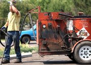 A warning sign on the truck reads "hot" as Stan Hofer from Blacktop Inc. wipes his brow as he works on sealing cracks at the St. Stephen's parking lot with his cousin, David Hofer, Friday in Billings, Mont. Billings broke a record Friday as temperatures hit 104 degrees.