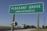 A small bouquet of flowers hangs form the road sign at Pleasant Grove, where two workers were killed Tuesday. Ramona Morgan and her, daughter, Sabrina Morgan, are suspects in the deaths.