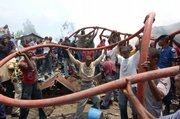 Local volunteers pass a fire hose to help firefighters douse debris at the site of a cargo plane crash Thursday in Kinshasa, Congo. A cargo plane smashed into a residential neighborhood in Congo's capital just after takeoff from the international airport Thursday, killing at least 25 people and engulfing homes in flames.