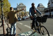 A man hitchhikes while another rides his bicycle Thursday in Paris. A public transport strike billed as France's biggest in years was in full swing, with commuters forced to walk, pedal or drive to work in large numbers, and many are thought to have stayed home.