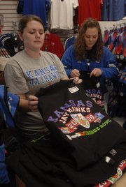 Jock's Nitch employees, from left, Amie Worthington and Kelsey Allen quickly fold some of the T-shirts that became available Monday for Kansas University's Orange Bowl appearance Jan. 3 in Miami. To get to the game, some travel packages cost $2,000.