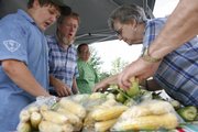 From left, Nolan, 12, and Galen and Marcia Peters, of Lawrence, sell sweet corn during the Lawrence Farmers' Market in the 1000 block of Vermont Street. On the right, Virginia Short, of Lawrence, picks out which ears of corn she wants.