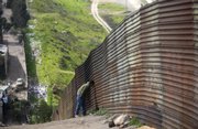 A man peeks through the border fence to the U.S. from Tijuana, Mexico, in this February 2008 file photo. Remittances sent home by Mexicans working abroad have fallen for six straight months, threatening local businesses and choking off what used to be a strong cash flow for many Mexican families.