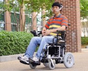 Graduate student Xueliang Huo glides down a walkway in a wheelchair that's controlled by a tiny magnet glued to his tongue. He is helping develop a system that turns the tongue into a joystick that controls wheelchairs and other electronics.