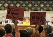 Protesters hold up signs as lawmakers, seen in background, question financial leaders, not pictured, at a Senate Banking Committee hearing this week on Capitol Hill in Washington.