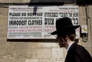 An ultra-Orthodox man walks past a sign calling on women to dress modestly Sept. 12 in a religious neighborhood in Jerusalem. In Israel's ultra-Orthodox Jewish community, where the rule of law takes a back seat to the rule of God, religious zealots are on a crusade to stamp out unchaste behavior.