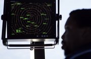 Air traffic controller Karl Haynes Jr. stands beneath a radar screen Sept. 18 in the control tower at Washington's Reagan National Airport. A satellite-driven network, dubbed NextGen, would save fuel by ditching World War II-era radar technology and enabling GPS-equipped planes to fly the shortest route between two points: a straight line.