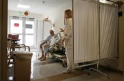 Nurse Nora Ledesma waves goodbye to patient Edward Gray after checking his vital signs on his bed last week in the hallway of Stony Brook University Hospital in Stony Brook, N.Y. Hospital officials across the nation are being urged to consider using hallways as a way to ease emergency department crowding, and some are trying it.