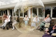 LeeAnn Blevins, left, director of activities at Regal Estates in Independence, Kan., assists Bruce Williams with blowing bubbles while residents Bonnie Bynum, Jayne Swepston, Vera Woods and Rose Bramble watch a giant bubble created by middle school students float by in this 2006 file photo.
