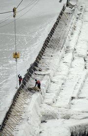 Bowersock Mill and Power Company workers rebuild a network of boards and doors Tuesday that hold back the Kansas River to enable the dam to generate more power.