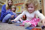 Teacher Nicole Reno holds 2-year-old Ava Wagner as they watch Davalin James, 2, build a house with plastic pieces at the Ballard Community Center.