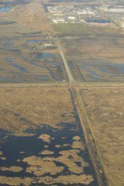 Development of additional wetlands at the southern edge of Lawrence is visible in this aerial photo, which looks west down North 1250 Road toward Iowa Street, which runs from left to right near the top of the photo. The bridge that marks the eastern end of the South Lawrence Trafficway is in the upper left corner; the large building with the dark roof in the upper right is Wal-Mart, 3300 Iowa. Cutting across the center of the photo from left to right is the extension of Louisiana Street. Above that is an area of new wetlands, to be planted this spring and summer. At the bottom: the existing Baker Wetlands, including an original, never-before-plowed area at the bottom left.