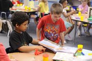 New York School kindergarten teacher Kim Gamble’s class spends some time making model dinosaurs. From left, Tristan Chavez, 6, works on a model, and Cody Daigle, 6, reads a book.