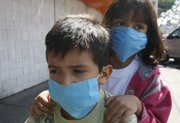 Hiram Diaz, 8, left, gives his 6-year-old sister Adely Diaz a ride on the pegs of his bicycle Saturday while wearing protective masks near the market where their parents own a store in Mexico City. Mexico is struggling with a new strain of swine flu that is showing up in parts of the U.S., including central Kansas.