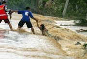 A woman holds on to a man as strong currents pull her away from the streets Friday in Rosales town, northern Philippines. Hundreds of people have been killed in the country’s worst flooding in 40 years after back-to-back storms started pounding the country’s north Sept. 26.