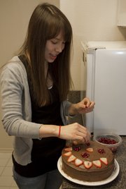 Nina Riley decorates the top of a chocolate frosting white cake with strawberries and pomegranate. Riley and her roommate blog together their cooking recipes.