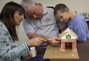 Marisa Dallman, from left, her husband, Kurt, and son, Erik, 6, attach red chewing gum for the siding of their gingerbread barn.