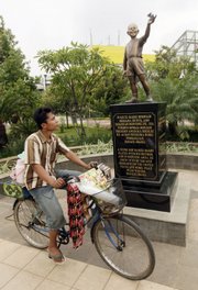 A coffee vendor on Tuesday rides past the statue of U.S. President Barack Obama as a 10-year-old boy at Menteng Park in Jakarta, Indonesia. The statue has been targeted in a Facebook campaign by thousands who say it should be removed.