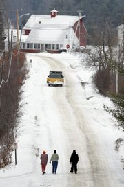 Women walk down a road Thursday in Vienna, Maine. The high cost of pavement has the town considering changing some of its 14 miles of paved roads back to gravel, which is cheaper to maintain.