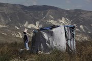 A woman left homeless by last month’s earthquake stands Friday next to her makeshift home on a hill overlooking Port-au-Prince. Prime Minister Jean-Max Bellerive said the Haitian government will appropriate privately held land to build temporary camps for earthquake victims.