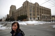 Biology teacher Nina Petrasek works at Vaux High School in Philadelphia, pictured in the background Monday. Petrasek says the school, which is cutting staff and lengthening the school day, is under-resourced and should start by fixing more basic problems than dismissing teachers.