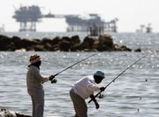 An oil-drilling platform stands offshore in the Gulf of Mexico as people fish Wednesday in Port Fourchon, La. A worker on an oil rig can expect cushy benefits but life-threatening labor.