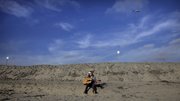 Michael Clower plays his guitar on the beach Wednesday as a U.S. Navy helicopter, top right, circles overhead less than a mile from the border with Tijuana, Mexico, in San Ysidro, Calif., on the outskirts of San Diego. As politicians say more federal troops are needed to fight rising violence along the U.S.-Mexico border, government data obtained by the Associated Press show the area actually isn’t so dangerous after all.