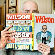 Daniel Clowes, at his home in Oakland, Calif., shows off his latest graphic novel, “Wilson.” It features a character who hangs around the coffee shops on Oakland’s Grand Avenue, verbally sucker punching strangers with whom he instigates one-sided conversations.