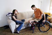 Brandon Hildebrand, right, moves to the couch to watch TV with his wife, Wendy, in this May 28 photo inside their Hutchinson home. Brandon and Wendy Hildebrand have had to reorganize their lives after a motorcycle accident left Brandon paralyzed.