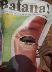 A child peers through a newspaper front page as patrons gathered to cheer on South Africa in the World Cup. South Africa beat France, 2-1, on Tuesday in Bloemfontein, South Africa, but failed to qualify for the next round.