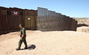 U.S. Border Patrol agent Santos Flores walks in front of the old border fence, back left, where it meets a five mile section of new border fence at the border in Nogales, Ariz., in this June 19, 2008, file photo. President Barack Obama’s plan to hire 1,000 more Border Patrol agents and other immigration officers could end up flooding the U.S.-Mexico border’s already overwhelmed federal courts, a judiciary official said Friday.