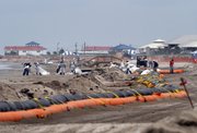 Workers shovel and bag sand contaminated with oil from the Deepwater Horizon oil rig explosion and spill, beyond a tiger dam on a beach Monday in Grand Isle, La.
