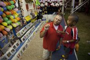 Carnival worker James Moore shows Keyon Free, 4, of Lawrence, how to hold a dart before an attempt to pop a balloon for a prize Thursday.