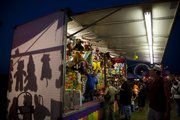 Shadows of hanging prizes are cast as carnival-goers browse the stands of Moore’s Greater Shows Carnival on Thursday.