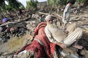 Pakistani flood-affected villagers sit Friday in the rubble of their houses, in Aza Kheil near Peshawar, Pakistan. International aid for Pakistani flood victims is coming in slowly compared with other recent disasters despite the massive number of people affected and the potential for dire economic consequences in a country key to Western hopes in the fight against Islamist extremists.