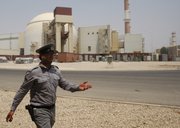 An Iranian security guard directs media Saturday at the Bushehr nuclear power plant, with the reactor building seen in the background, just outside the southern city of Bushehr, Iran.