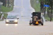 A buggy and car drive through high water Thursday on South Farmersville Road at Groff’s Creek in Ephrata, Pa. Much of eastern Pennsylvania is under flood warnings as storms could bring as much as six inches of rain before leaving the area today. The National Weather Service issued a tornado watch Thursday for counties stretching from Philadelphia west to York and north to Allentown.
