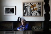 Artist John Crawford, son of artist Ralston Crawford, sits Oct. 8 in his living room with his father’s abstract photo “Leaves,” left, and painting “St. Gilles,” in Brooklyn, New York. Also pictured are John Crawford’s own sculptures “Arch of Sphere,” left, and “Tower 2,” right.