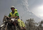 Villagers ride on a motorcycle Saturday as Mount Merapi spews volcanic materials in the background in Srumbung, Central Java, Indonesia.