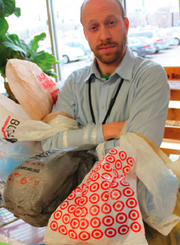 Brian Phillips, store operations manager at The Merc, stands with a collection of 60 plastic bags, the average number of bags a family of four gathers in one month. At the request of the food cooperative's owners, the store will no longer offer plastic bags for packing groceries.