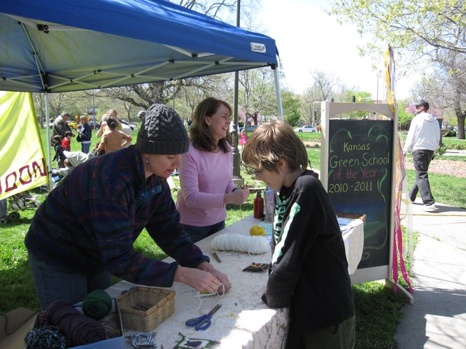Prairie Moon Waldorf School, which recently was named a Kansas Green School of the Year, had a booth at the Earth Day Celebration in South Park. From left, Dana Atwood-Blaine and Amy Stevenson, teach Raiden Garcia, 11, Lawrence, how to make a God's Eye. It is made from yarn and two sticks.