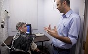 Kansas University associate professor of social psychology, Omri Gillath talks with Journal-World reporter Shaun Hittle, who is wearing a net of electrodes used for measuring brain waves relative to Gillath's research in measuring one's willingness to be generous, Thursday, June 23, 2011, at a lab in Fraser Hall.
