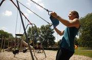Laura Webb, a personal trainer at Kansas University's student recreation center, demonstrates pulls on a swing at Watson Park.