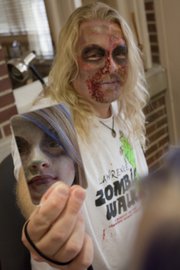 Harold Agnew holds a mirror so his daughter, Parvaneh Karch-Agnew, can see the "zombie face" that makeup artist Elahe Marjovi painted on her. Marjovi also did makeup on Agnew, the organizer of this year&squot;s Lawrence Zombie Walk. The walk takes place on Thursday, Oct. 6, and benefits the Lawrence Humane Society.