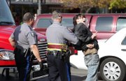 An Occupy Lawrence protester signals a peace sign to the crowd while being taken away by Lawrence Police after he was removed from the roof of Weaver's department store downtown during a rally Saturday, Nov. 5, 2011.