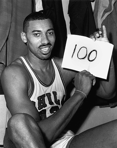 In this file photo from March 2, 1962, Wilt Chamberlain of the Philadelphia Warriors holds a sign reading “100” in the dressing room in Hershey, Pa., after he scored 100 points as the Warriors defeated the New York Knickerbockers, 169-147.