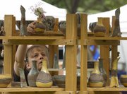 Cynthia Schmidt, Paola, places a vase on a display shelf as she sets up her booth at Art in the Park. Cloudy skies threatened rain all day, but the downpour held off until the event’s closing time.