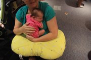 One-week-old Maggie Stultz, above, rests in her mother’s lap. Nursing a baby can be cumbersome, but moms and babies can get a boost with the help of a Boppy, a U-shaped pillow that slips around a mother’s waist and helps support the baby.