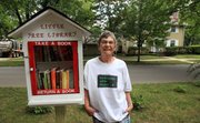 C.J. Brune stands next to a shelf stocked with books in her front yard that anyone can come by and borrow a book from, an endeavor inspired by the Little Free Library project.